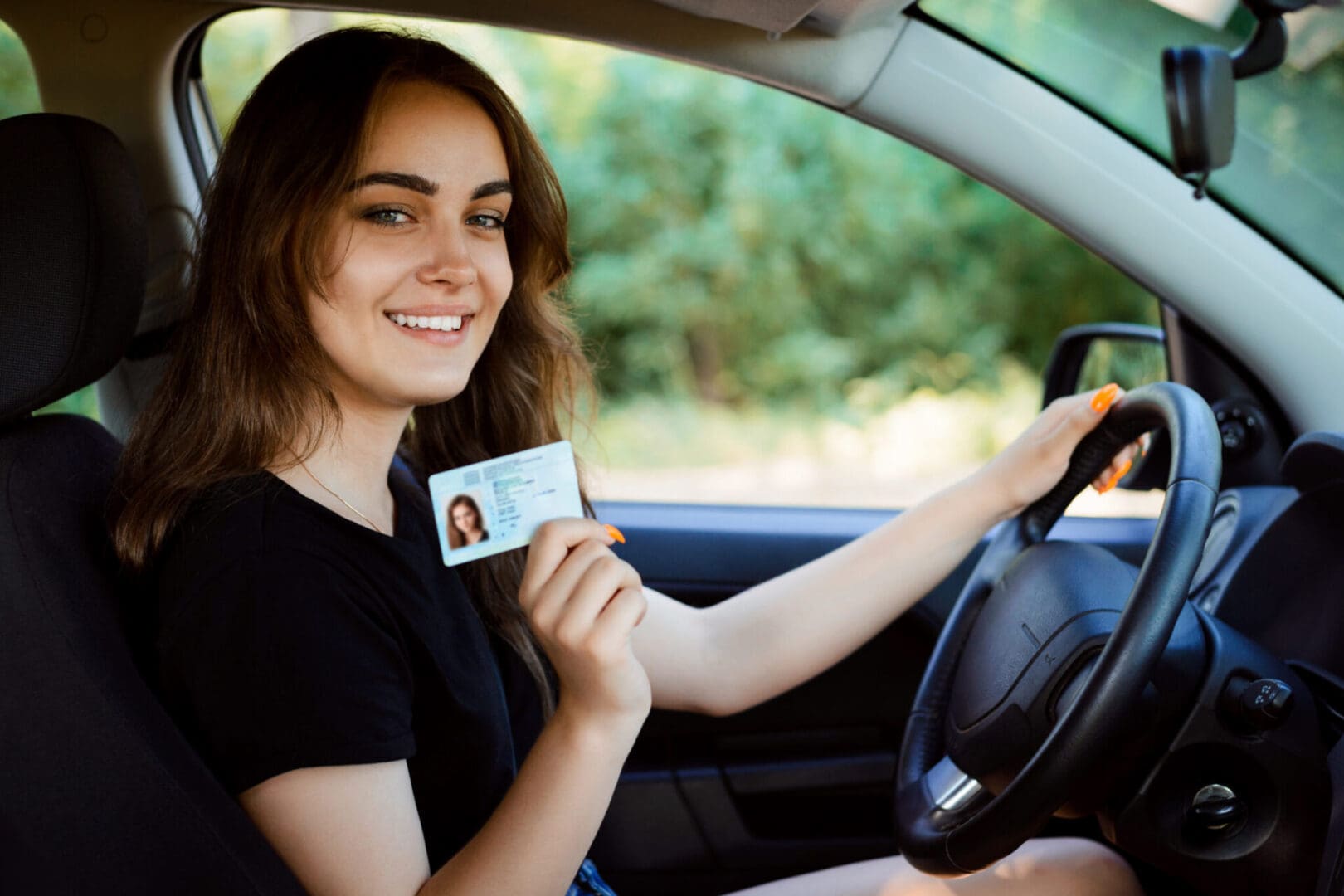 A woman sitting in her car holding up an id.